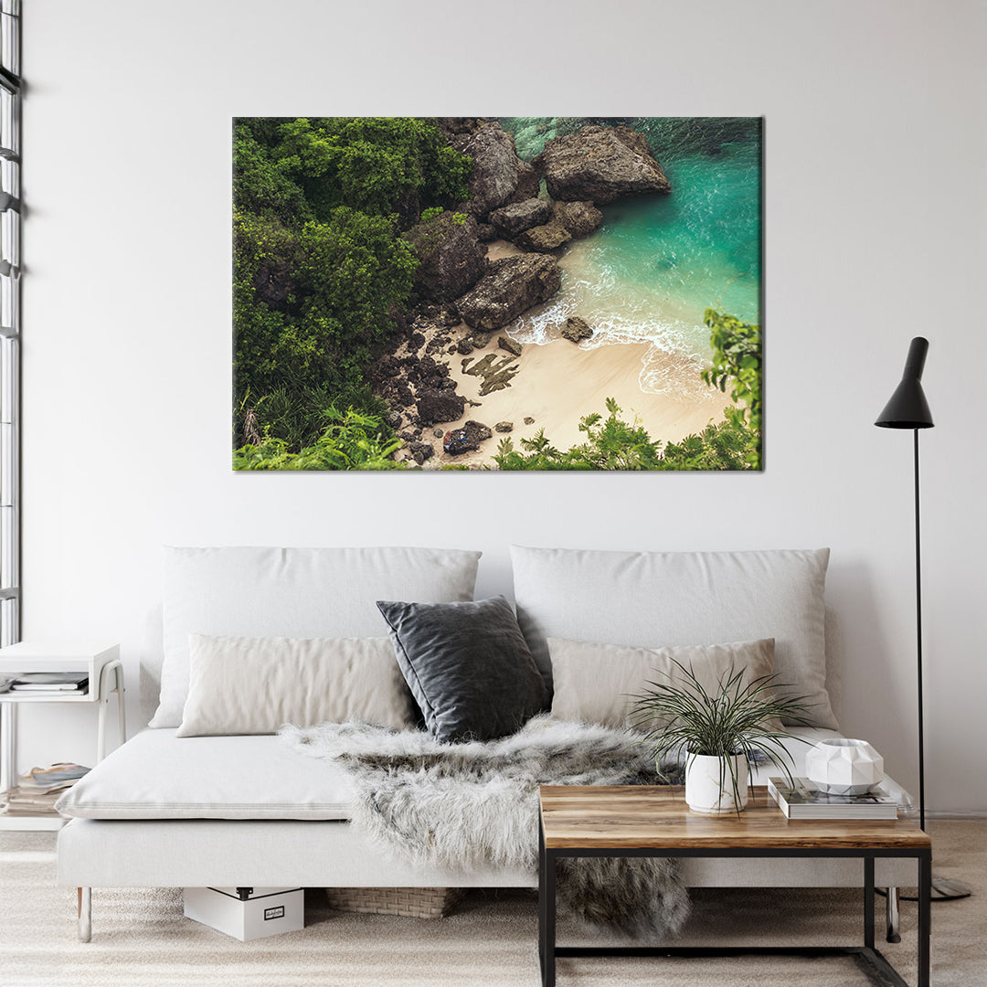 White sand beach beside big black stones and green water Framed Canvas